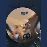 Kulatý mosazný činel s kladivkovaným povrchem. Na horní části je černý nápis Mb10 a pod ním text 16" Medium Crash, v horní části je viditelné logo ME…