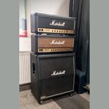 Sada kytarového komba značky Marshall v černém provedení, složená ze dvou zesilovačů a jednoho reproduktorového boxu. Všechny tři části mají bílý lem…