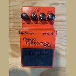 Kytarový efekt pedál oranžové barvy s modrým spínacím tlačítkem. Na přední straně je nápis Mega Distortion MD-2 a na spínači vyražené logo BOSS. V ho…
