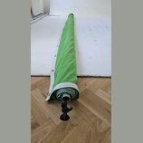 Zelený textilní kryt s bílým okrajem, který je navinutý na kovovou tyč. Na konci tyče je černý plastový utahovací šroub s knoflíkem. Povrch textilu v…