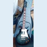 Elektrická kytara typu Les Paul s tmavě modrým průhledným lakem a viditnou strukturou dřeva. Na hlavě je bílé logo Cort, na hmatníku jsou bílé blokov…
