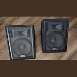 Dva černé reproduktory v hranatých bednách s kovovými ochrannými mřížkami. Na spodní části mřížek je umístěno logo s nápisem Soundking. Povrch beden…