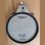 Kruhový elektronický trigger pad v šedé a černé barvě s kovovým uchytem. Na horní části je nápis PD-85 DUAL TRIGGER PAD a na membráně logo Roland s d…
