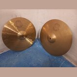 Dva mosazné činely s jemným rýhováním povrchu. Oba mají v horní části vyryté logo SOUND FORMULA. Levý činel má nápis Medium Heavy HiHat Bottom 14, pr…