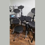 Elektronická bicí souprava v černé barvě s černými pady a činely. Na několika padych je viditelný nápis ARLSBROG, stejný nápis je i na pedálech. Souč…