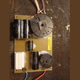 Fotografie znázorňuje elektronickou desku s osazenými komponenty. Na desce jsou čtyři černé válcové kondenzátory s bílým nápisem BENNIC, dva z nich m…
