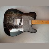 Elektrická kytara s černým bodies, které je zdobeno šedými paisley vzory. Hned vedle snímače se nachází malý červený nápis "Made in USA". Hmatník je…