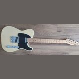 Elektrická kytara s krémovým korpusem, černým pickguardem a světle hnědým hmatníkem. Na hlavě krku je nápis Fender TELECASTER. Nástroj vykazuje čistý…