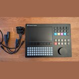Černý sampler Polyend Tracker s displejem, mřížkou bílých podsvícených polí a ovládacím knoflíkem. Na horní hraně je bílý nápis Polyend Tracker s log…