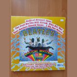 Fotografie zobrazuje obal vinylové desky s nápisem BEATLES a názvem alba MAGICAL MYSTERY TOUR. Na obalu jsou čtyři postavy v kostýmech opic na barevn…