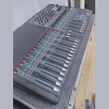 Šedočerný mixovací pult s posuvníky a řadou ovládacích knoflíků. V levém horním rohu je bílý nápis Soundcraft a vedle něj označení modelu SX. Zařízen…