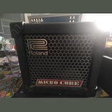 Černý kytarový kombo zesilovač s kovovou mřížkou reproduktoru. Na přední straně je umístěno logo Roland a nápis MICRO CUBE v červeném rámečku. Povrch…