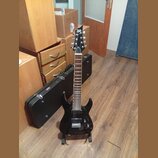 Černá elektrická kytara s špičatou hlavou a dvěma humbuckery, umístěná na stojanu. Na hlavě je bílé logo Ltd. Kytara má tmavý hmatník s bílými poloho…