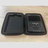 Černý přenosný sekvencer Polyend Tracker Mini v černém zipovém pouzdře. Na horní hraně přístroje jsou nápisy Polyend a Tracker Mini. Ovládací panel o…