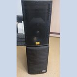 Černý reproduktor s kovovou mřížkou, na které je umístěn žlutý štítek s nápisem SPL Acoustics. Reproduktor stojí na černém polstrovaném podstavci, ve…