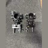 Dvě černé kovové svorky pro upevnění příslušenství. Každá svorka se skládá z horního kruhového úchopu a spodního stahovacího mechanismu s chromovaným…