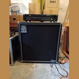 Černý basový kombozesilovač s bílým lemováním a černou textilní maskou. V levém horním rohu je logo Ampeg a v pravém dolním rohu nápis CLASSIIC. Na h…
