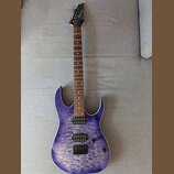 Elektrická kytara s modrým průsvitným povrchem s výraznou strukturou dřeva. Na hlavě hmatníku je viditelné logo Ibanez. Nástroj má dva humbuckery, je…