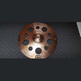 Kulatý mosazný činel s koncentrickými drážkami na povrchu a několika průchozími otvory různých velikostí. V horní části je nápis „HCS“ a pod ním menš…