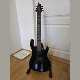Černá elektrická kytara s dvojsekmem, umístěná na černém stojanu. Na hlavě nástroje je bílý nápis CORT. Kytara má dva humbuckery a dva ovládací knofl…