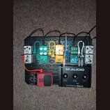 Na černém efektovém pedalboardu je umístěno šest kytarových pedálů a jedno audio rozhraní. Zleva doprava jsou řazeny pedály s nápisy AD-6, VALETON TU…