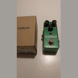 Zelený efekt pedál s nápisem OVERDRIVE a tři černé ovládací knoflíky s popisky DRIVE, LEVEL a TONE. Nad nápisem se nachází malá červená kontrolka. Ve…
