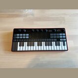 Černý analogový syntetizátor s červeným rámem a bílo-černou klaviaturou. V pravém horním rohu je logo LUNA a nápis SYNTH PRO, v horní části uprostřed…