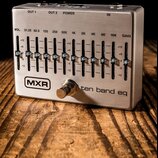 Stříbrný kytarový pedál s nápisem MXR a ten band eq. Zařízení obsahuje deset posuvníků pro ekvalizaci s označením frekvencí od 31.25 do 16K, dále reg…