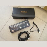 Černý efektový pedál s nápisem M-WAVE a řadou bílých otočných ovladačů. Pod ovladači jsou popisy: VOLUME, IN CAB, REVERB, MIX, FX, TIME, MOD, TONE, G…