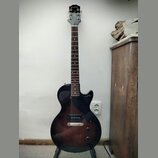 Elektrická kytara s tmavě hnědým gradientem (sunburst) a černým hmatníkem. Na hlavě je bílý nápis Epiphone. Nástroj má dva humbuckery, jeden tónový a…