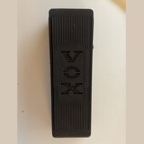 Černý obdélníkový pedál s povrchem z rýhované gumy. Uprostřed je vyryto logo VOX a nápisy AMPLIFIER a INSTRUMENTS. Povrch vykazuje mírné známky opotř…