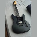 Černá elektrická kytara s matným povrchem a černým pickguardem. Na hlavě hmatníku je viditelné logo Fender. Nástroj má jeden humbucker v pozici kobyl…