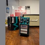 Kytarový efekt v zeleném kovovém krytu s nápisy Ibanez, TS9B a Bass Tube Screamer. Na horní části jsou čtyři ovládací knoflíky s popisky DRIVE, LEVEL…