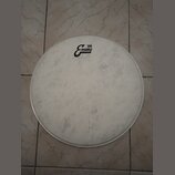 Bílá kruhová bubenová kože v kovovém obruči. Na pravé straně je černé logo s nápisy „Evans“ a „'56“ a menším textem „CRAFTED IN USA“. Povrch kože vyk…