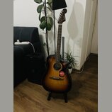 Akustická kytara s korpusem v tmavě hnědém sunburst provedení a dřevěným hmatníkem. Na hlavě nástroje je bílý nápis Fender. Na těle kytary je nalepen…