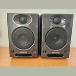 Dva identické studiové monitory v tmavě šedém lesklém provedení. Každý reproduktor má v horní části menší výšký reproduktor a ve spodní části větší b…