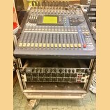 Digitální mixážní pult značky YAMAHA, model OXY 5, umístěný v transportním case. Zařízení má šedé tělo s modrými prvky, LCD displej a řadu posuvníků.…