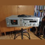 Stříbrný kazetový přehrávač s nápisem AKAI STEREO CASSETTE DECK Model GX-F80. Přístroj obsahuje vložení kazety, ovládací tlačítka a dva velké bílé ov…