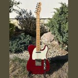 Elektrická kytara typu Telecaster v červené barvě s bílým pickguardem a světle hnědým javorovým hmatníkem. Na hlavě je viditelné logo Fender. Povrch…
