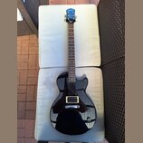 Černá elektrická kytara s tmavým hnedým hmatníkem a černým pickguardem. Na hlavě je bílý nápis Epiphone. Nástroj vykazuje známky běžného používání, p…