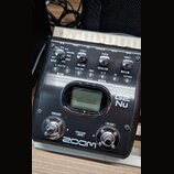 Černý efektový pedál značky ZOOM, model G2 Nu. Zařízení obsahuje displej, tři ovládací knoflíky s popisky PARM 1, PARM 2 a PARM 3, několik tlačítek a…