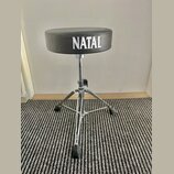 Černý bubeníckýstolek s kulatým polstrovaným sedadlem. Na přední straně sedadla je bílý nápis NATAL. Nohy a středový sloupek jsou vyrobeny z chromova…