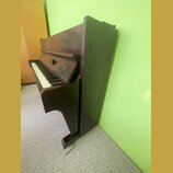 Tmavně hnědé digitální piano s dřevěnou texturou povrchu. Nástroj má klasický tvar s klaviaturou a integrovaným stojanem. Na viditelných částech nejs…