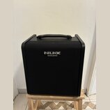 Černý akustický kombozesilovač s texturovaným povrchem a přenosnou úchytkou z umělé kůže. Na přední straně je umístěno logo NUX a pod ním nápis ACOUS…
