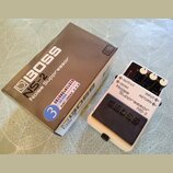 Bílé efektové pedál s černým spínacím tlačítkem a třemi ovládacími knoflíky. Na pedálu je nápis BOSS Noise Suppressor NS-2 a označení vstupů OUTPUT,…