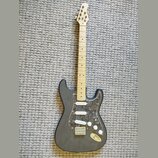 Černá elektrická kytara s tvarem typu Stratocaster a tři bílými snímači. Nástroj má světlý dřevěný hmatník a plech s tmavým mramorovaným vzorem. Na h…