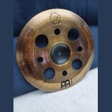 Kruhový činel z mosazného kovu s několika otvory různých velikostí v ploše. Na povrchu jsou nápisy PURE ALLOY, CUSTOM a 12" TRASH CHINA spolu s logem…