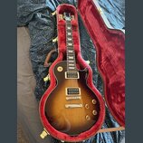 Elektrická kytara s trupem ve tvaru Les Paul v barevné variantě sunburst, umístěná v otevřeném tvrdém kufru s červeným polstrováním. Nástroj má dva h…