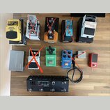 Fotografie zobrazuje sadu kytarových efektů a příslušenství na dřevěném povrchu. V horní řadě jsou pedály Graphic Equalizer EQ700, TONEX a Boss Chrom…