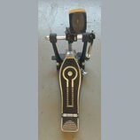 Fotografie znázorňuje černý bicí pedál s kovovými prvky. Na šlapadle je vidět dekorativní stříbrné vlnité rýhování a geometrický ornament s kruhem. N…